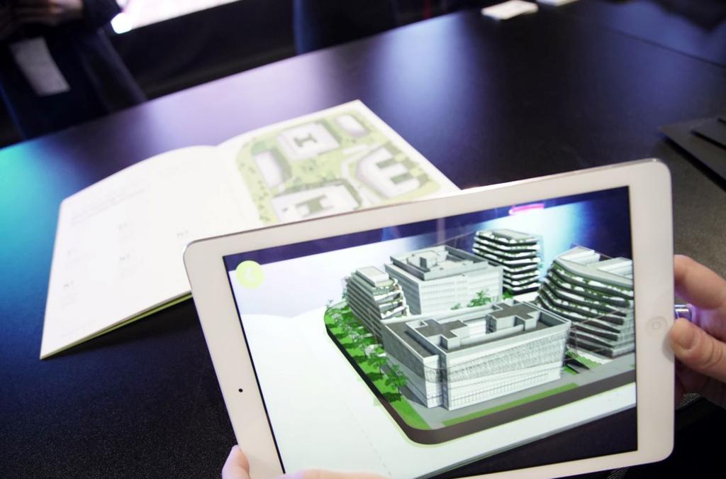 Close-up of a person holding an iPad displaying an augmented reality (AR) model of the GTC Green Heart Complex, overlaid on a physical brochure with the layout of the complex, demonstrating the innovative way of exploring real estate through AR technology.