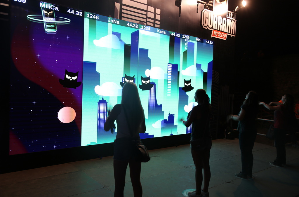 Participants focused on playing an interactive game at an event, standing in front of a large LED screen displaying an owl, part of a Guarana promotion.