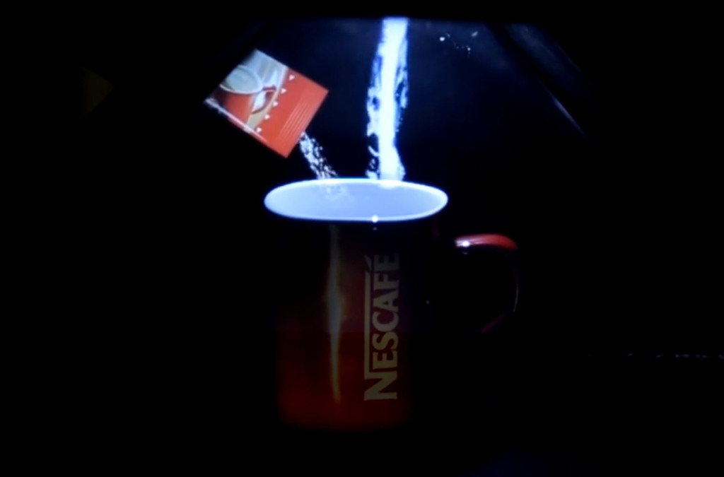 A holographic animation of a Nescafe 3 in 1 product packet pouring into the real Nescafe cup, demonstrating the use of mixed reality for product presentation within a hologram pyramid.
