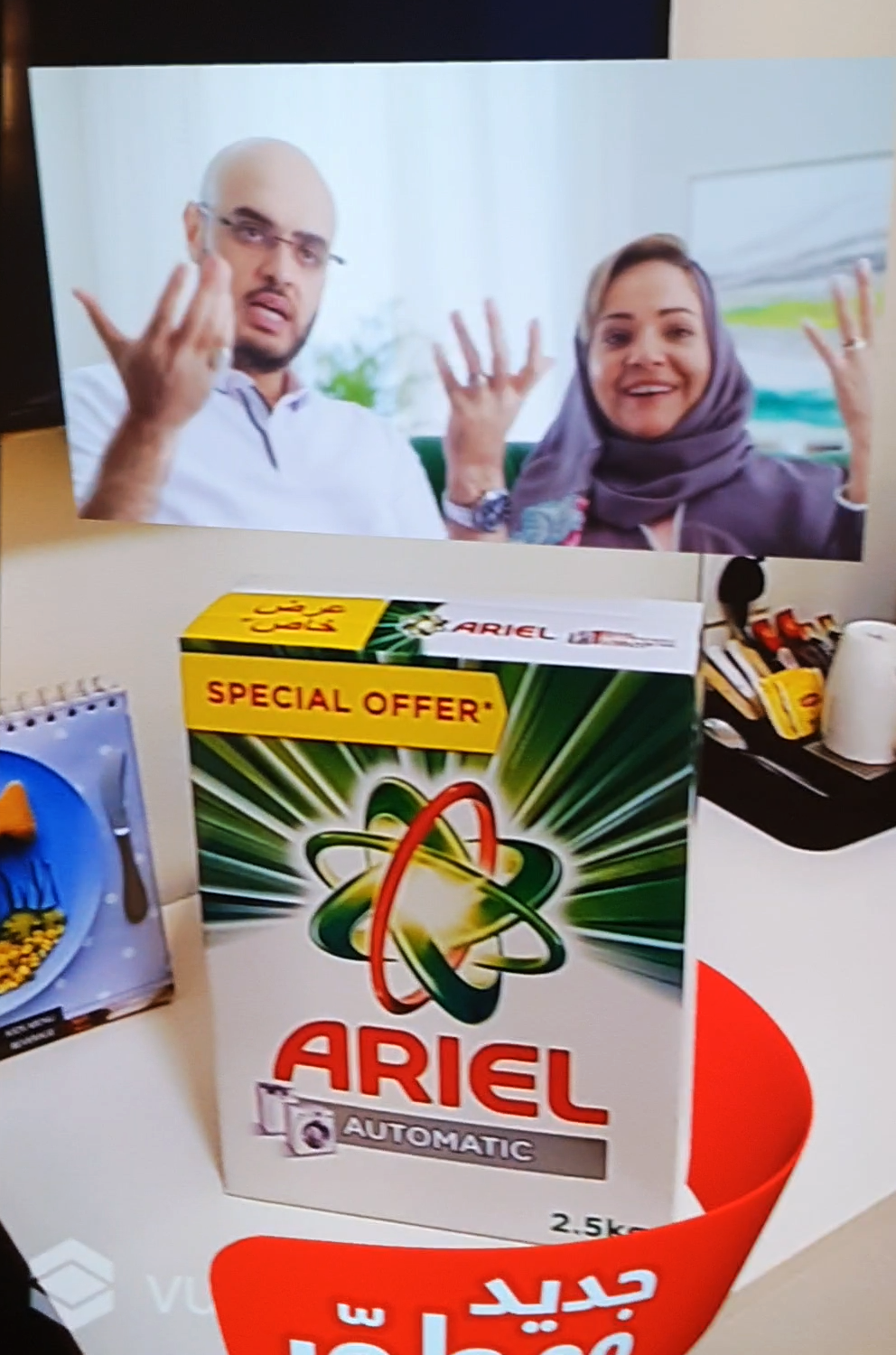 Close-up of a smartphone held in a hand, with the screen showing an augmented reality (AR) animation activated by scanning an Ariel laundry detergent box.