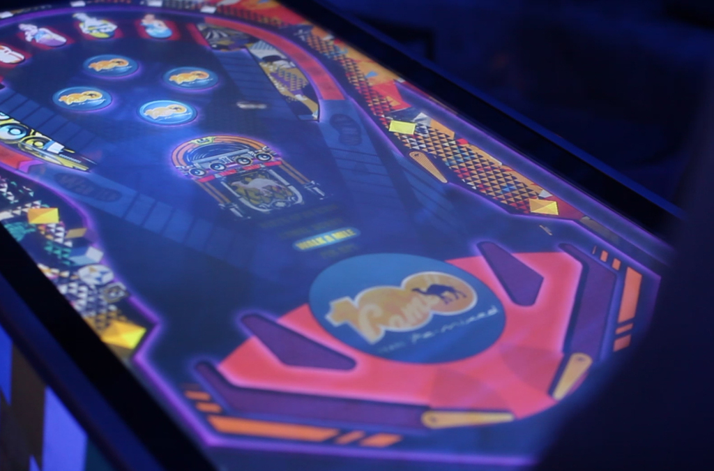 Detail of the Camel digital pinball game screen, glowing in the dark with vibrant colors and branding, representing a modern twist on the classic pinball experience.