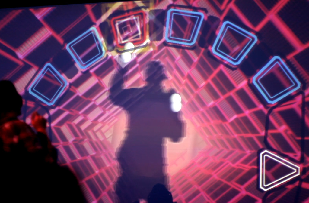 Silhouetted against a mesmerizing backdrop of a luminous virtual vortex, a person with headphones orchestrates music and visual effects with the motion of their body in an interactive VJDJ environment.