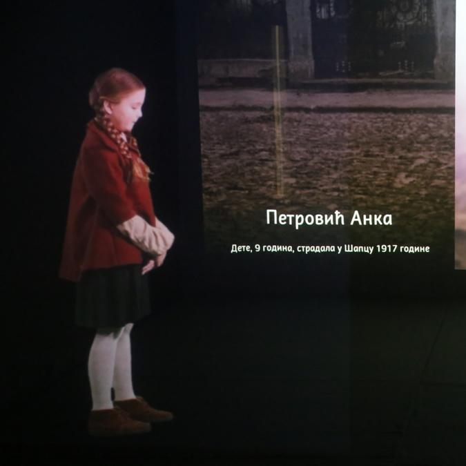 A life-sized hologram of a young girl, representing a WWI victim, stands in front of a projection displaying historical names and scenes.