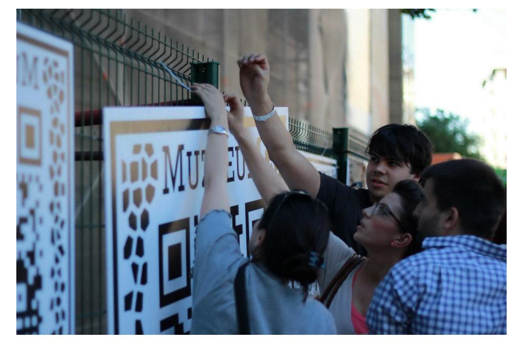 Visitors engage with the MUZZEUM project by scanning ARQR codes on placards with their smartphones, connecting to the virtual display of cultural artifacts.