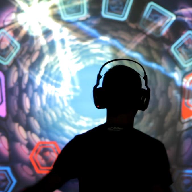Silhouetted against a mesmerizing backdrop of a luminous virtual vortex, a person with headphones orchestrates music and visual effects with the motion of their body in an interactive VJDJ environment.