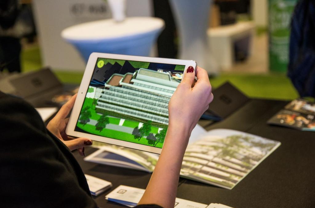 Close-up of a person holding an iPad displaying an augmented reality (AR) model of the GTC Green Heart Complex, overlaid on a physical brochure with the layout of the complex, demonstrating the innovative way of exploring real estate through AR technology.