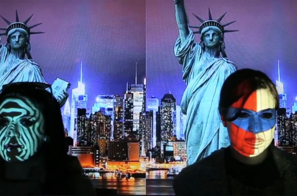 Two people participate in a real-time face mapping installation, with projections of New York City and the Statue of Liberty on their faces.