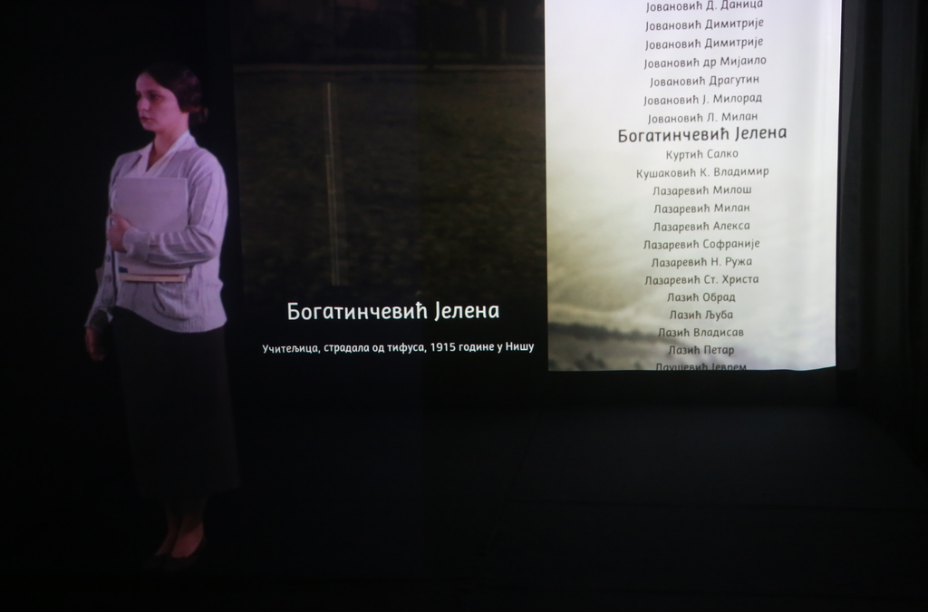 A life-sized holographic projection of a female WWI victim with a background listing historical names and details.