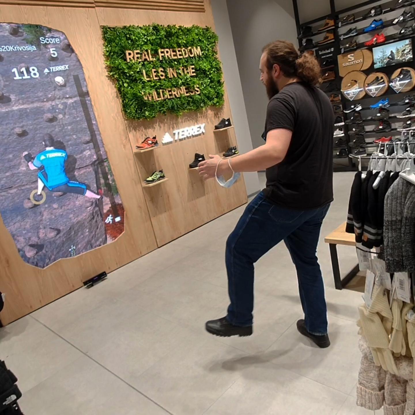 A player is actively engaging with the 'Sport Vision Climbing' interactive game in a store. They simulate climbing motions in front of a digital screen that displays a virtual rocky mountain terrain.