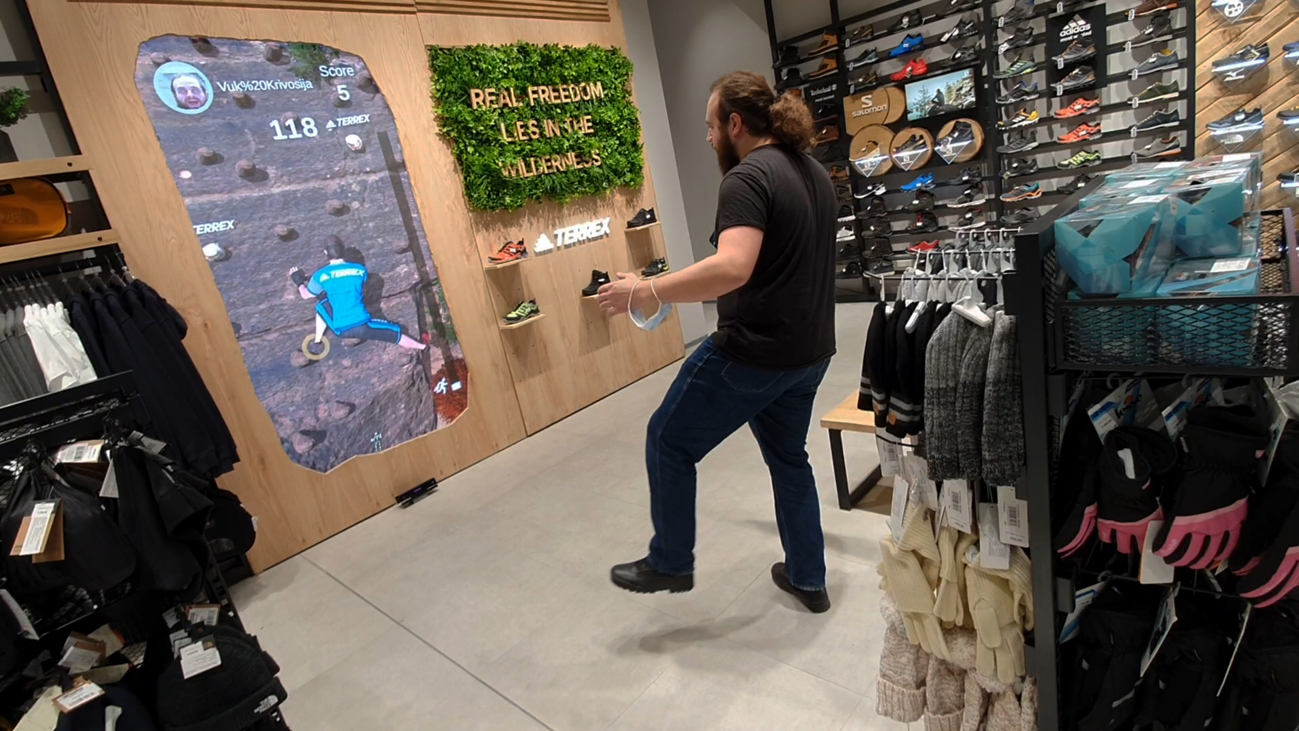 A player is actively engaging with the 'Sport Vision Climbing' interactive game in a store. They simulate climbing motions in front of a digital screen that displays a virtual rocky mountain terrain.