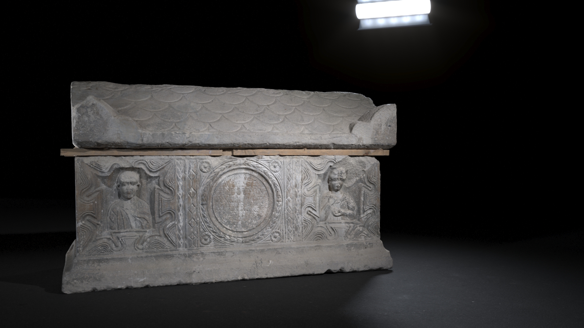 A horizontally oriented image of an elaborately decorated Roman sarcophagus featuring sculpted figures and patterns, with a partial fish scale design on the lid, showcased under bright lighting against a dark setting.