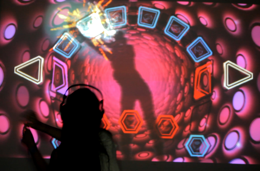 Silhouetted against a mesmerizing backdrop of a luminous virtual vortex, a person with headphones orchestrates music and visual effects with the motion of their body in an interactive VJDJ environment.