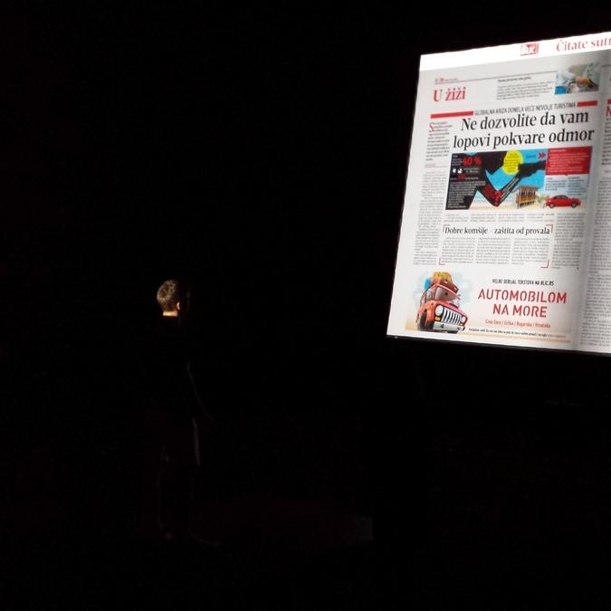 A person in a dark room using hand gestures to interact with a large projection of a digital newspaper, powered by Gesture Page Flipping software with a Microsoft Kinect sensor.