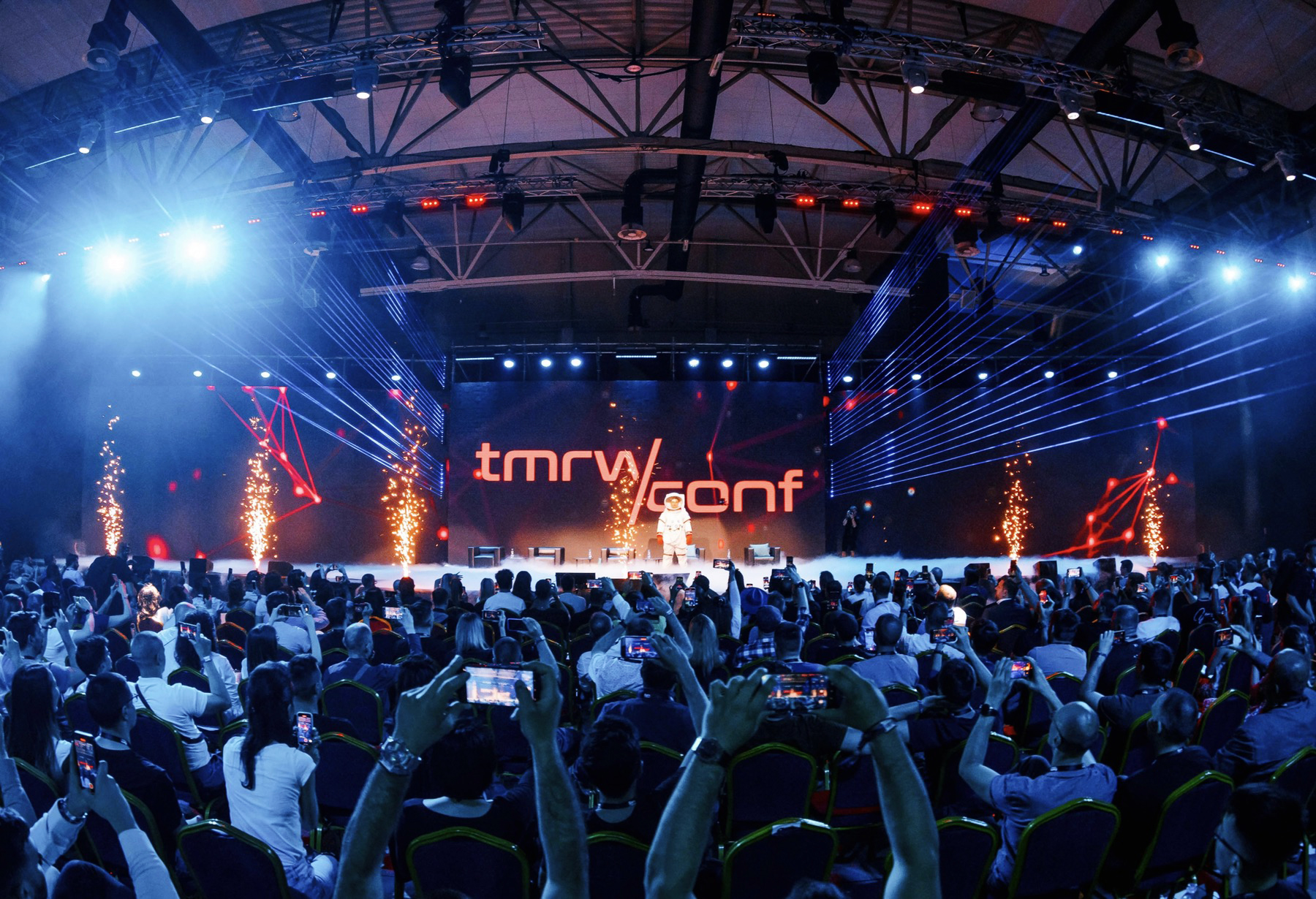 Attendees at the TMRW Conference in Belgrade watch a speaker on stage, surrounded by an impressive display of lights and visual effects, exemplifying the cutting-edge theme of NFTs and cryptocurrency.