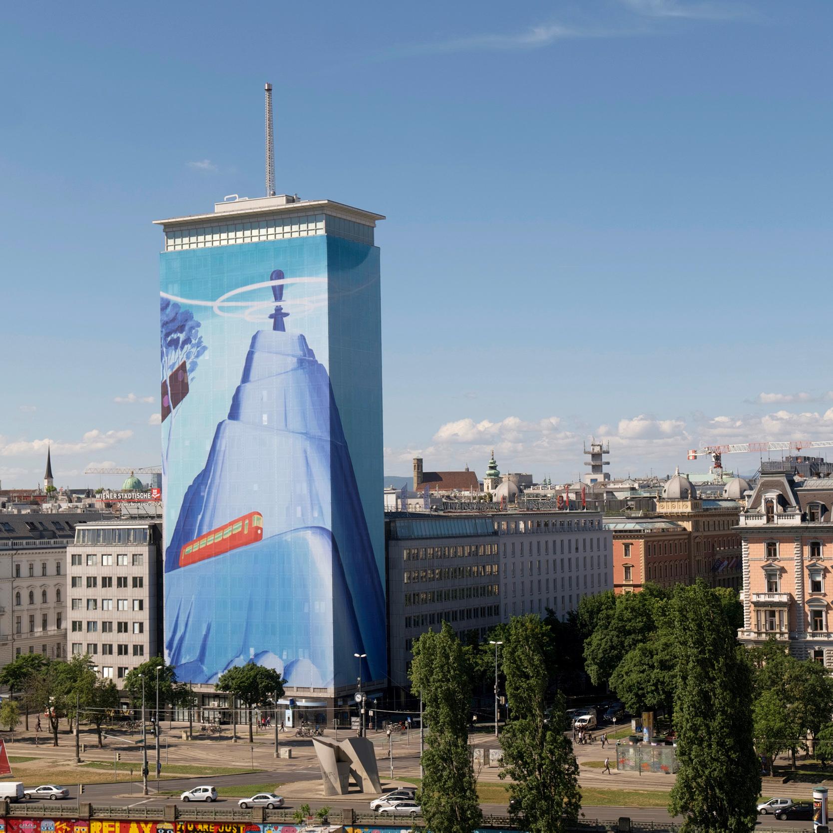 The Ringturm building in Vienna, wrapped in a colossal art installation portraying a blue-hued scene with satellite, space, and technology motifs, representing the Wiener Städtische's commitment to innovation. The surrounding urban landscape contrasts with the vibrant artwork.