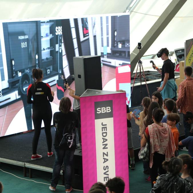 A lively scene at the Balkan TUBE Fest with attendees, mostly children, watching two players competing in an SBB VR game.