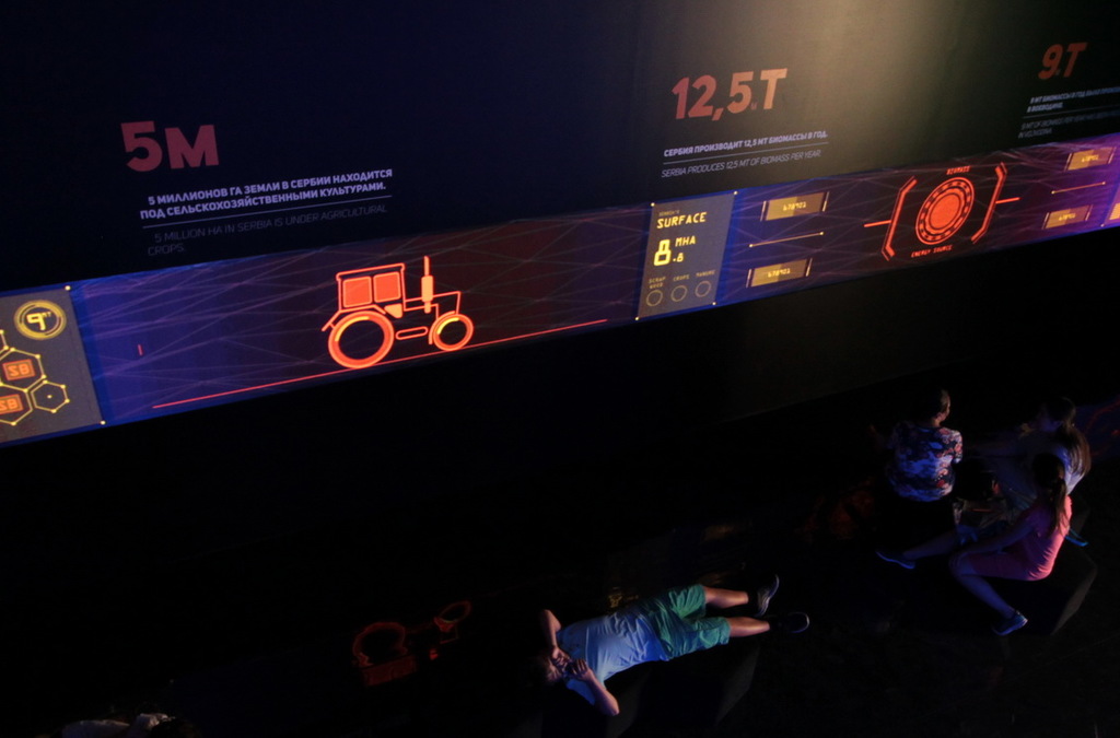 Visitors relax by an interactive screen demonstrating the use of biomass energy in Serbia.