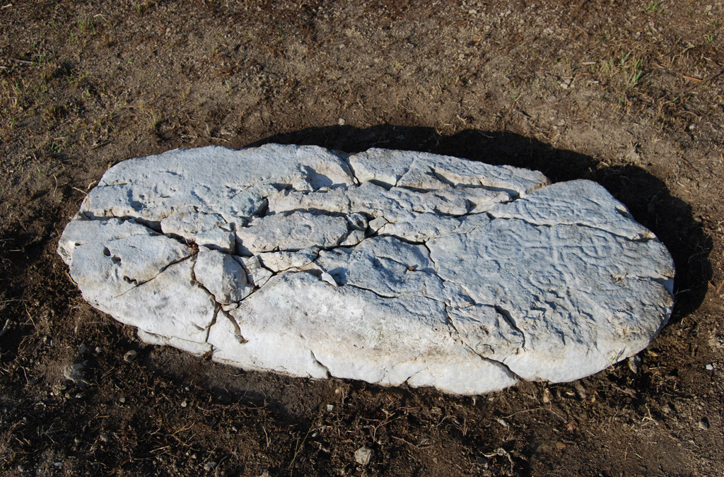 Photograph of an ancient, horizontal tombstone with surface erosion patterns, captured in natural daylight.