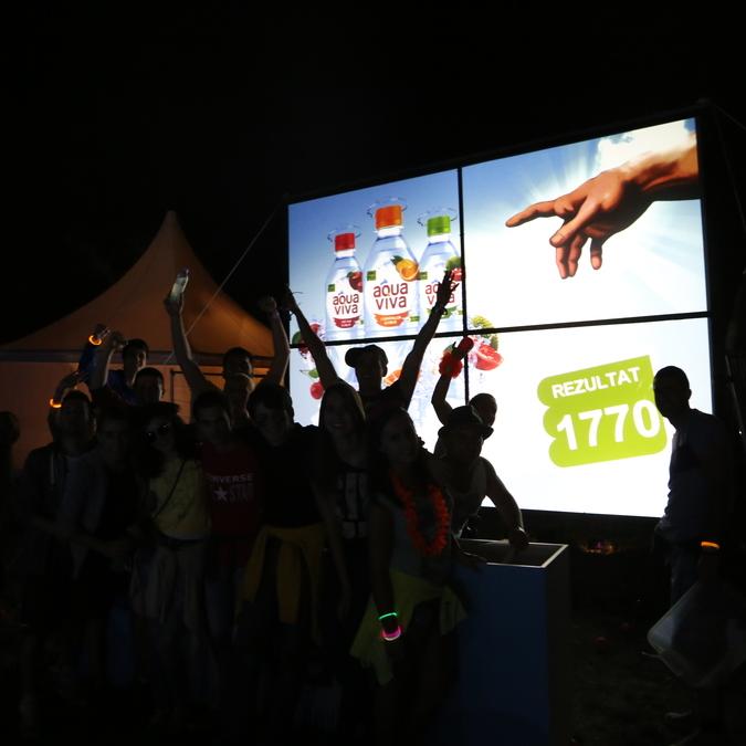 A group of festival-goers engages in a ball throwing game on a large multi-touch screen at the EXIT festival, part of an Aqua Viva brand activation.