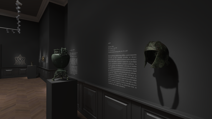 Interior of a dark-toned museum gallery with spotlighted exhibits including a green bronze cauldron with figural decorations on a pedestal and an ancient Corinthian helmet displayed on the wall, casting a shadow.