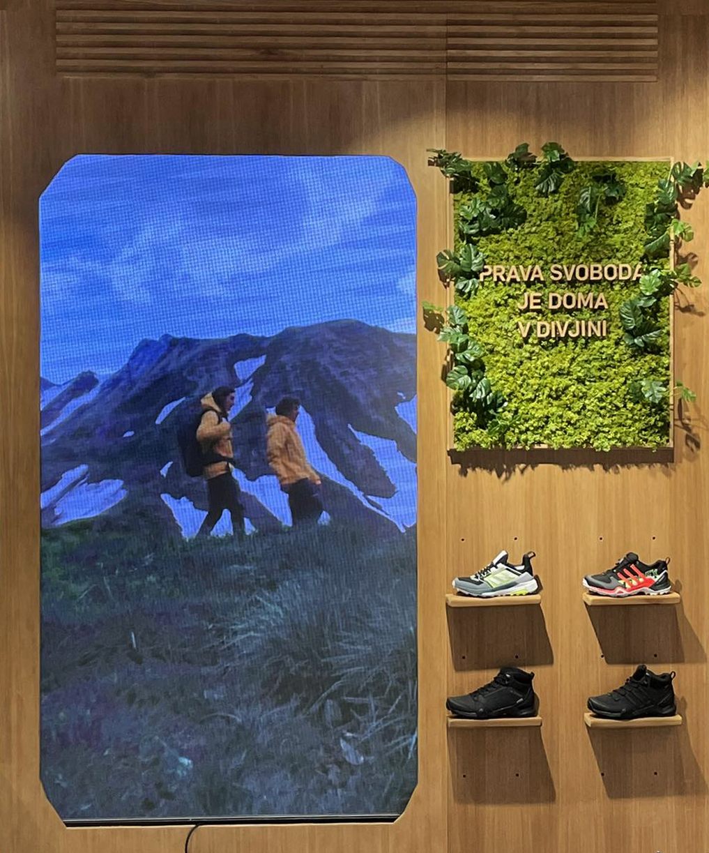 A digital interactive display for the 'Sport Vision Climbing' game, showing a simulated climbing environment with mountains and a climber avatar. Next to the screen is a vertical garden with the text 'Feel the Mountain,' and a selection of Adidas TERREX shoes displayed on shelves.