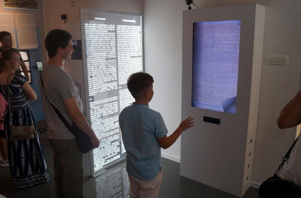 An image of visitors at the JUNUB exhibition interacting with the Kinect literary collection, where a young boy is engaging with a digital display showcasing the handwritten work of Petar Kočić.