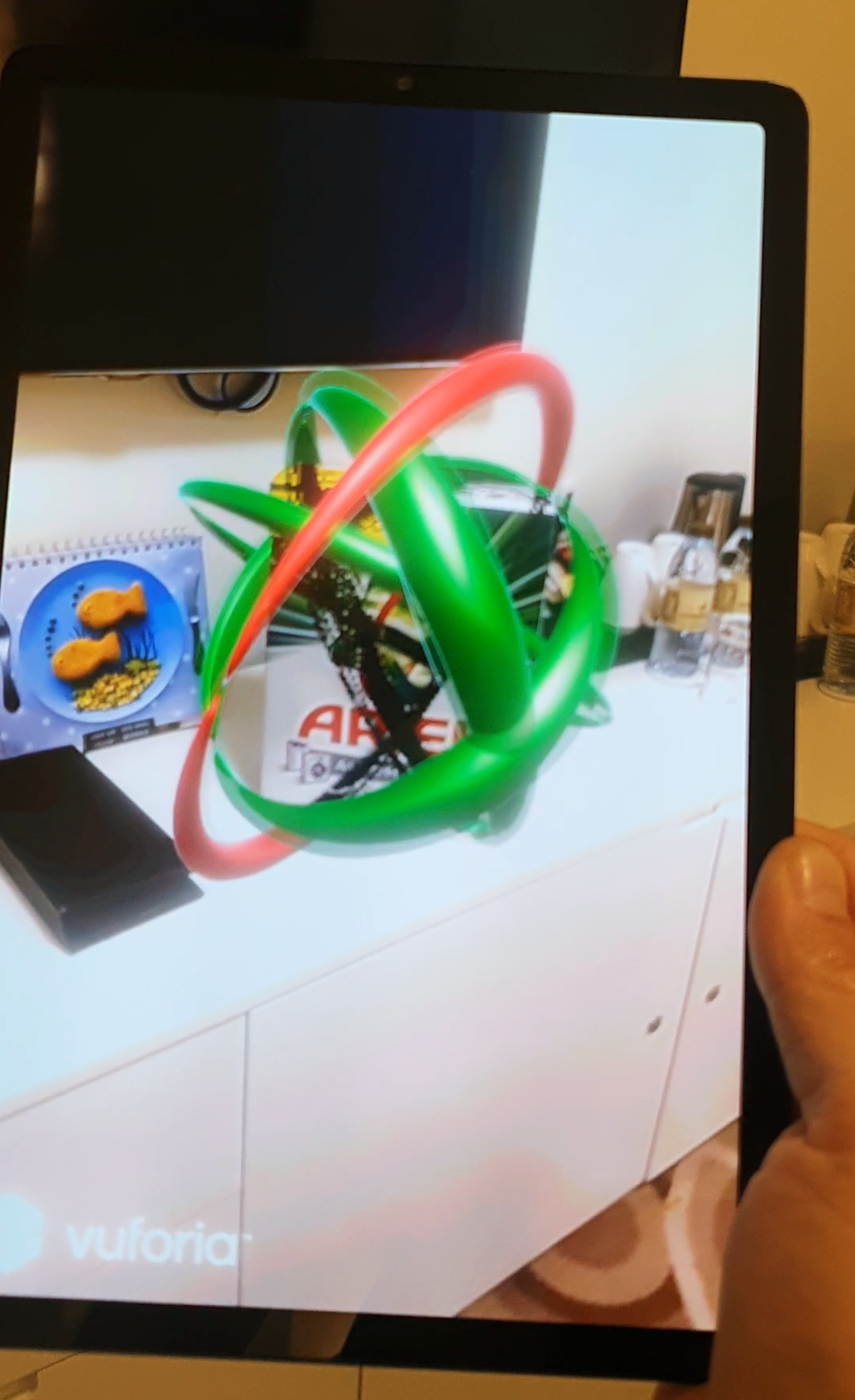 Close-up of a smartphone held in a hand, with the screen showing an augmented reality (AR) animation activated by scanning an Ariel laundry detergent box.