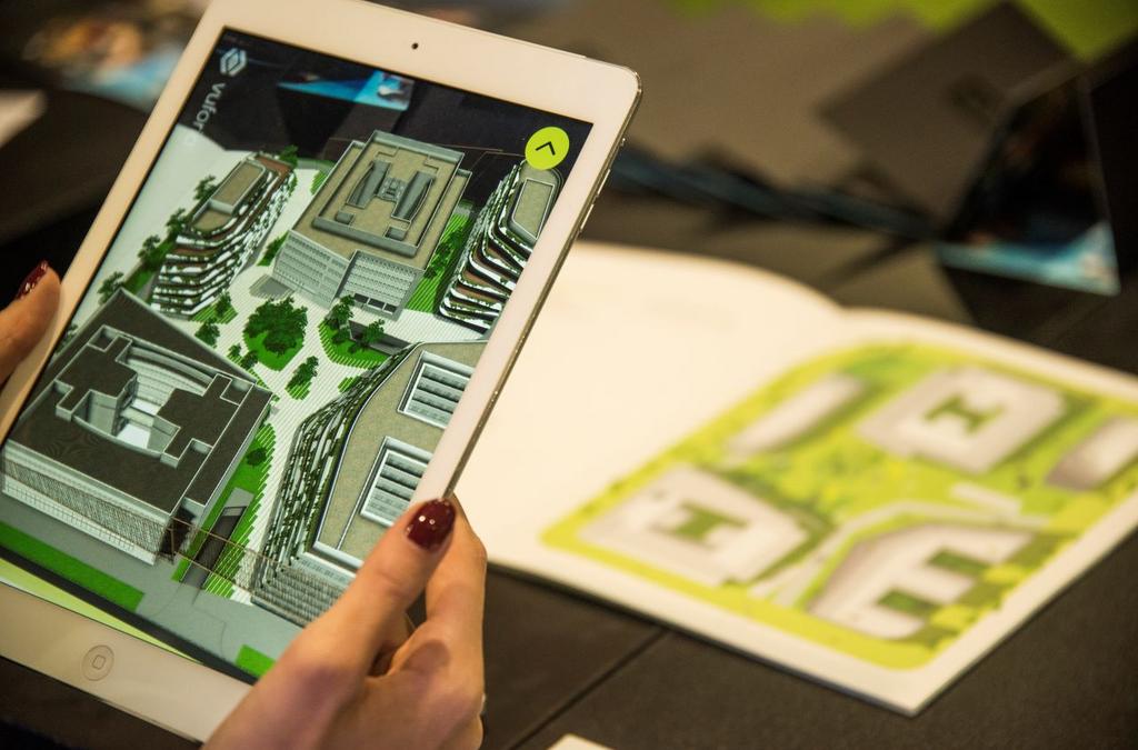 Close-up of a person holding an iPad displaying an augmented reality (AR) model of the GTC Green Heart Complex, overlaid on a physical brochure with the layout of the complex, demonstrating the innovative way of exploring real estate through AR technology.