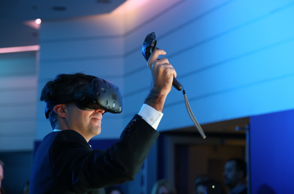 A VR participant is seen from the side, wearing a headset and holding a controller aloft, engaging with a virtual basketball gaming experience.