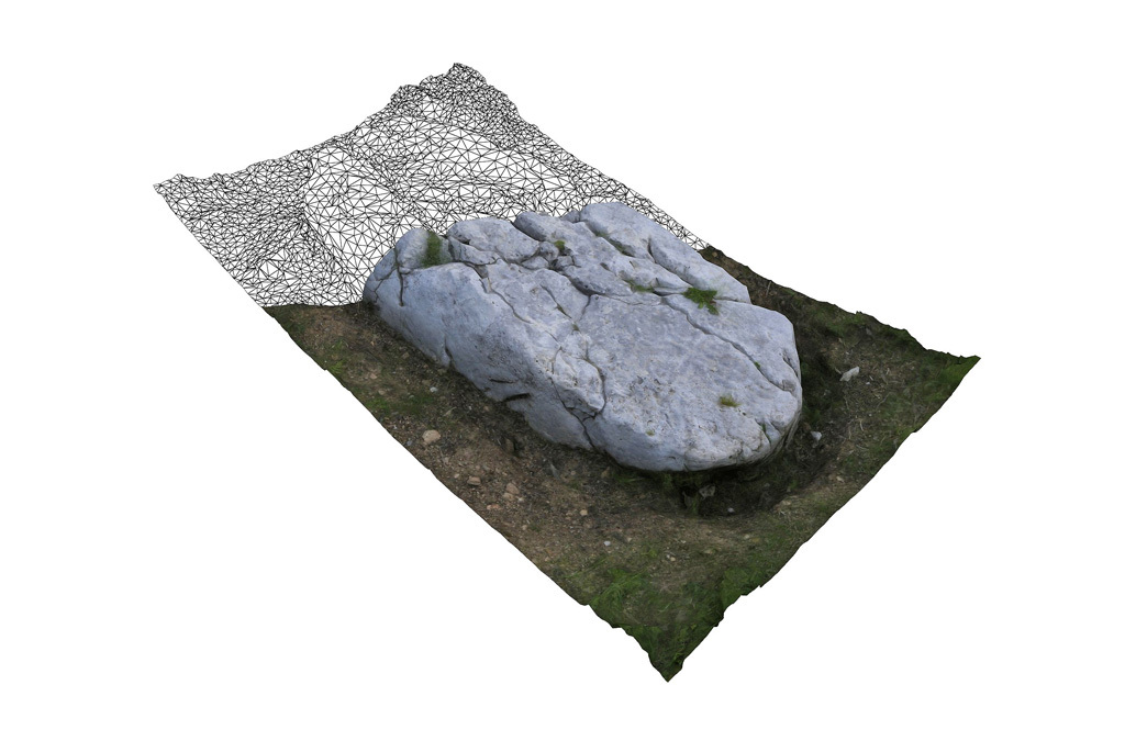 "3D scanned image of an irregularly shaped ancient tombstone with realistic textures on grass, partially overlaid with a wireframe grid.