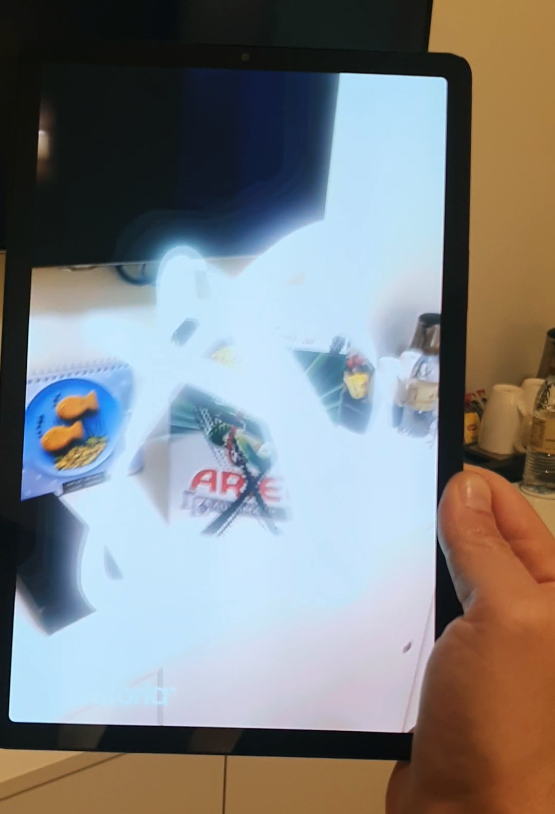 Close-up of a smartphone held in a hand, with the screen showing an augmented reality (AR) animation activated by scanning an Ariel laundry detergent box.