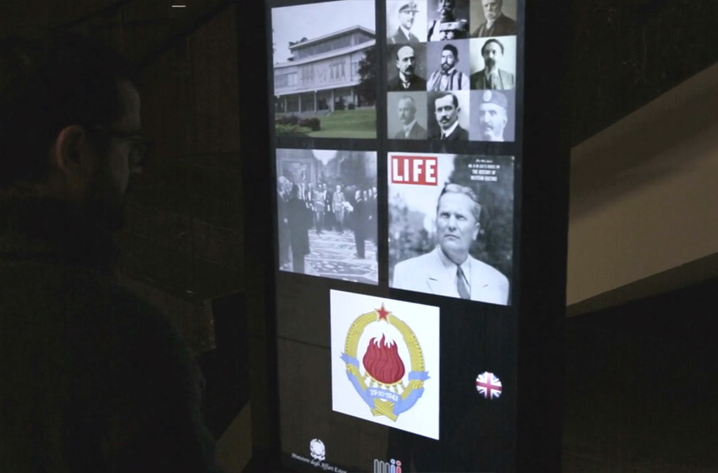 Interactive totem displaying historical images and information, with a visitor navigating through the digital content at the Museum of Yugoslav History.