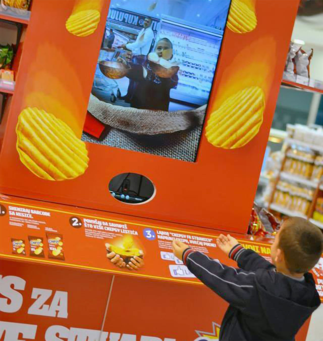 A young boy engaging with the Chipsy AR game, attempting to catch virtual chips projected on a screen in a supermarket setting.