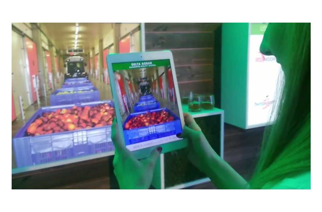 A person holds a tablet that overlays an augmented reality display of an apple's internal structure over a real image of a cart filled with apples, demonstrating an innovative way to learn about the product.