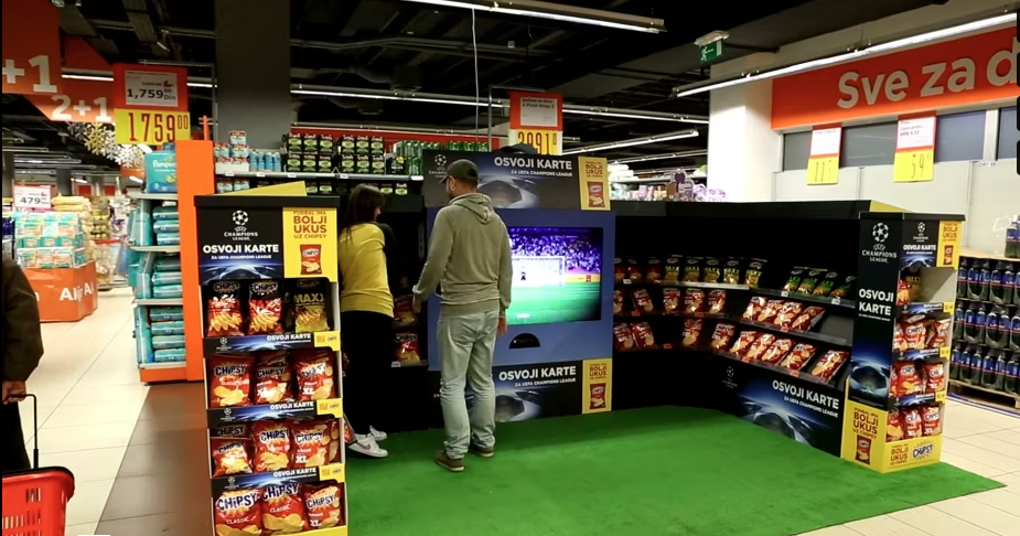 Customers engage with an interactive football game installation set up in a supermarket.