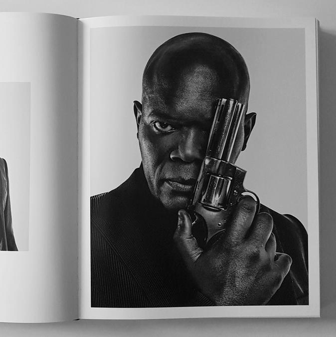 A monochrome photograph in a book depicting Samuel L. Jackson holding a revolver pointed directly at the camera, with an intense gaze, capturing a sense of drama and power.