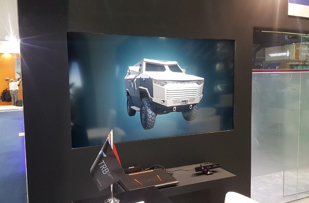A promotional display at IDEX 2019 featuring a digital rendering of the Despot 4x4 vehicle, presented on a large screen within a sleek exhibition booth with the TRB logo visible, illustrating the vehicle's futuristic design.