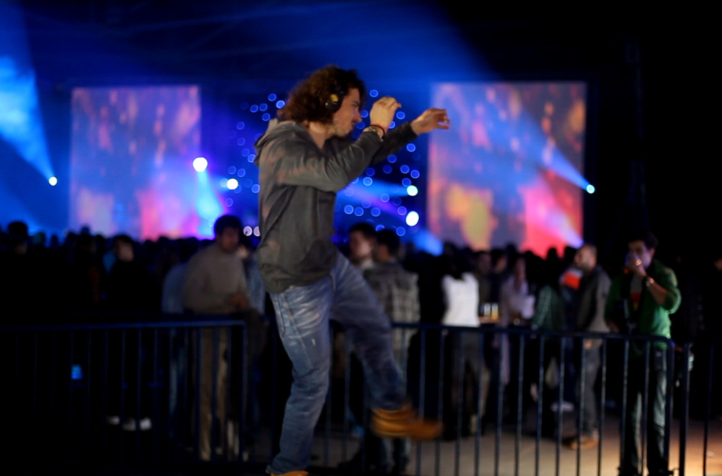An individual in the foreground gestures energetically towards a vibrant, colorful backdrop, interacting with a music and visual effects installation that transforms movement into sound.