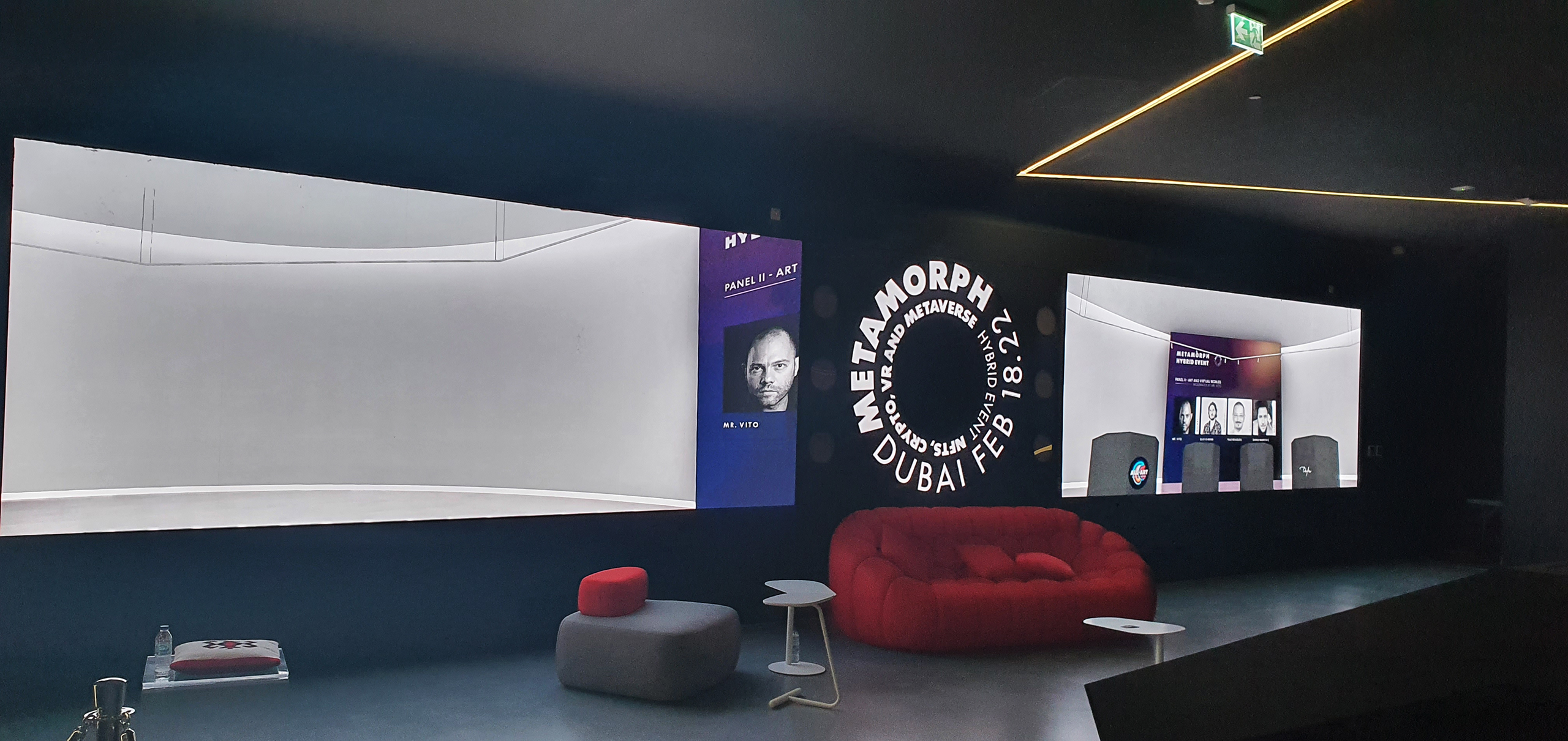 The interior of the Metamorph event venue displaying an immersive space with a modern, dimly lit lounge area. Monitors display the event’s branding and participant avatars, emphasizing the hybrid nature of the conference that combines live interactions with virtual reality experiences.