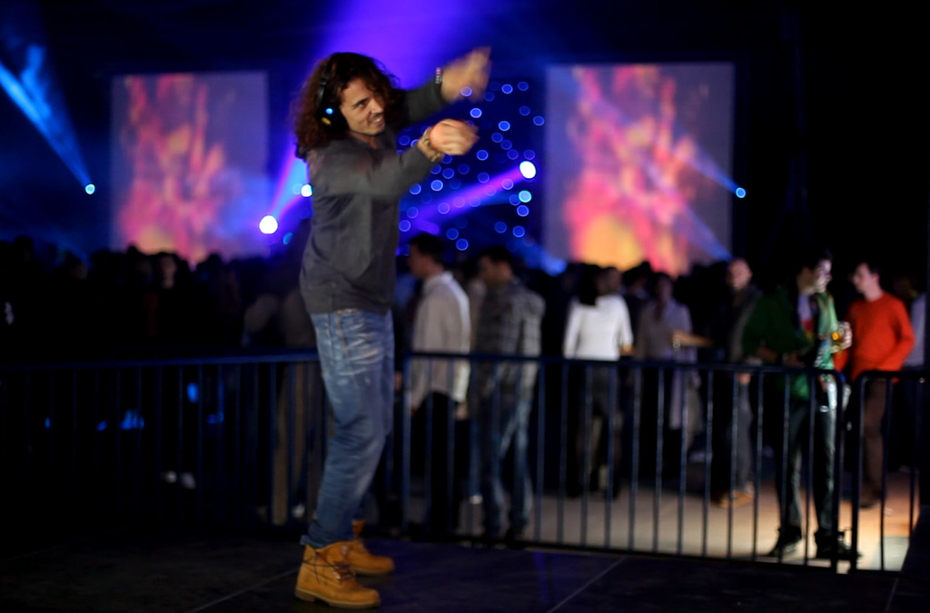An individual in the foreground gestures energetically towards a vibrant, colorful backdrop, interacting with a music and visual effects installation that transforms movement into sound.