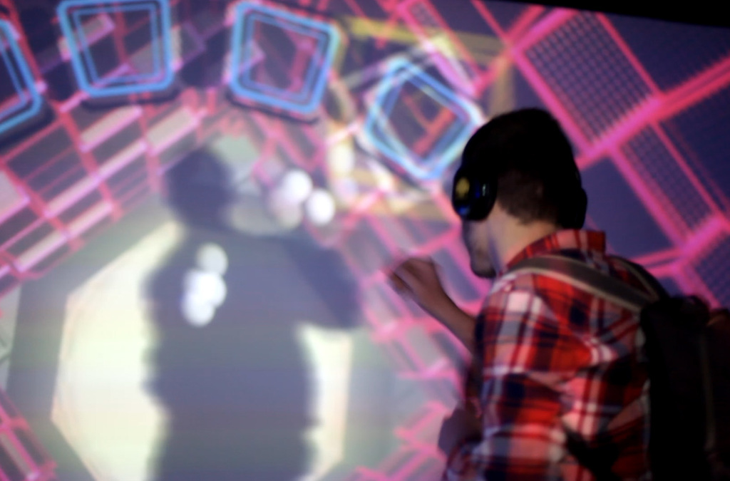 Silhouetted against a mesmerizing backdrop of a luminous virtual vortex, a person with headphones orchestrates music and visual effects with the motion of their body in an interactive VJDJ environment.
