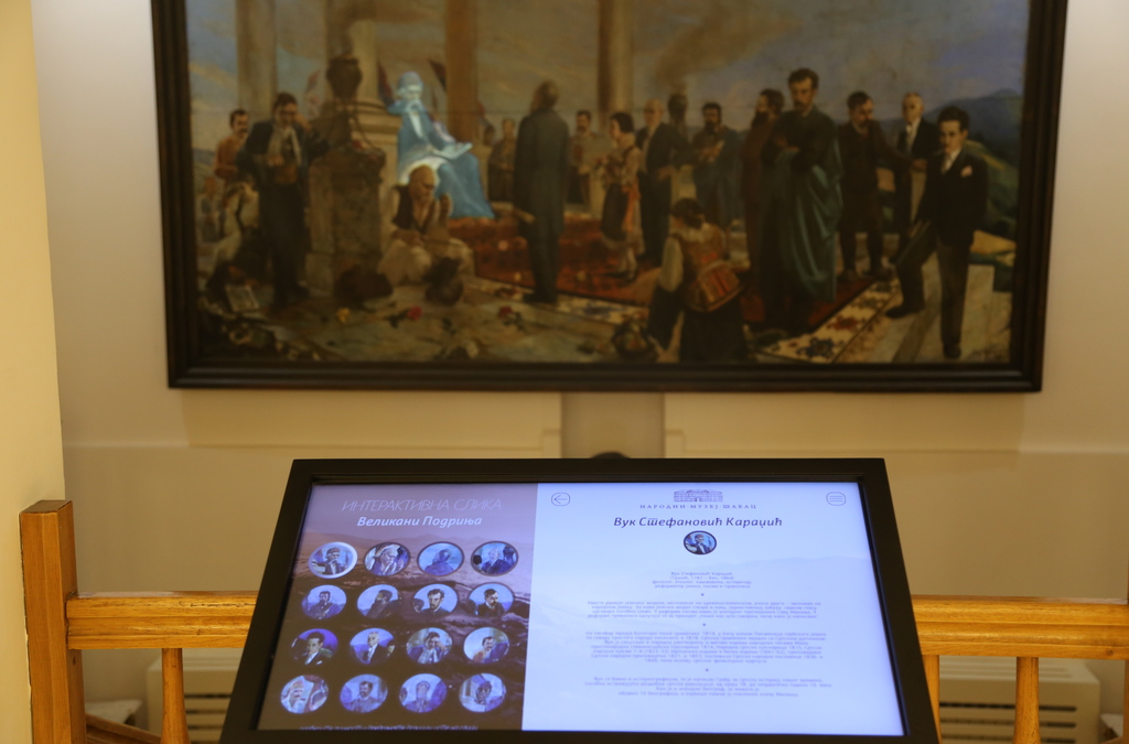 A multi-touch interactive display set against a historical painting allows museum visitors to learn more about the exhibit.
