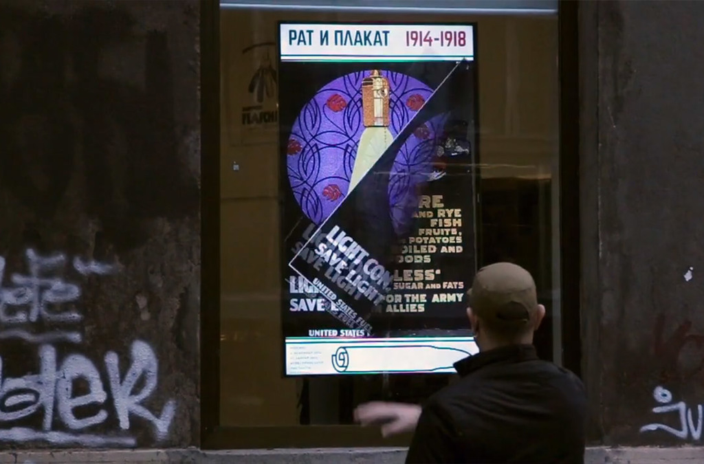 A man interacts with an interactive screen displaying a vintage war poster as part of the “Rat i Plakat” exhibition on the street.