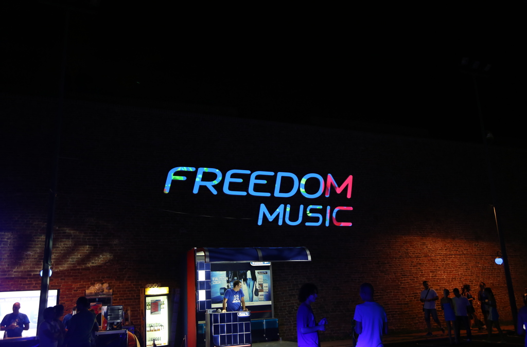 he words "FREEDOM MUSIC" projected onto a brick wall in stylized, glowing letters that appear to float in the air