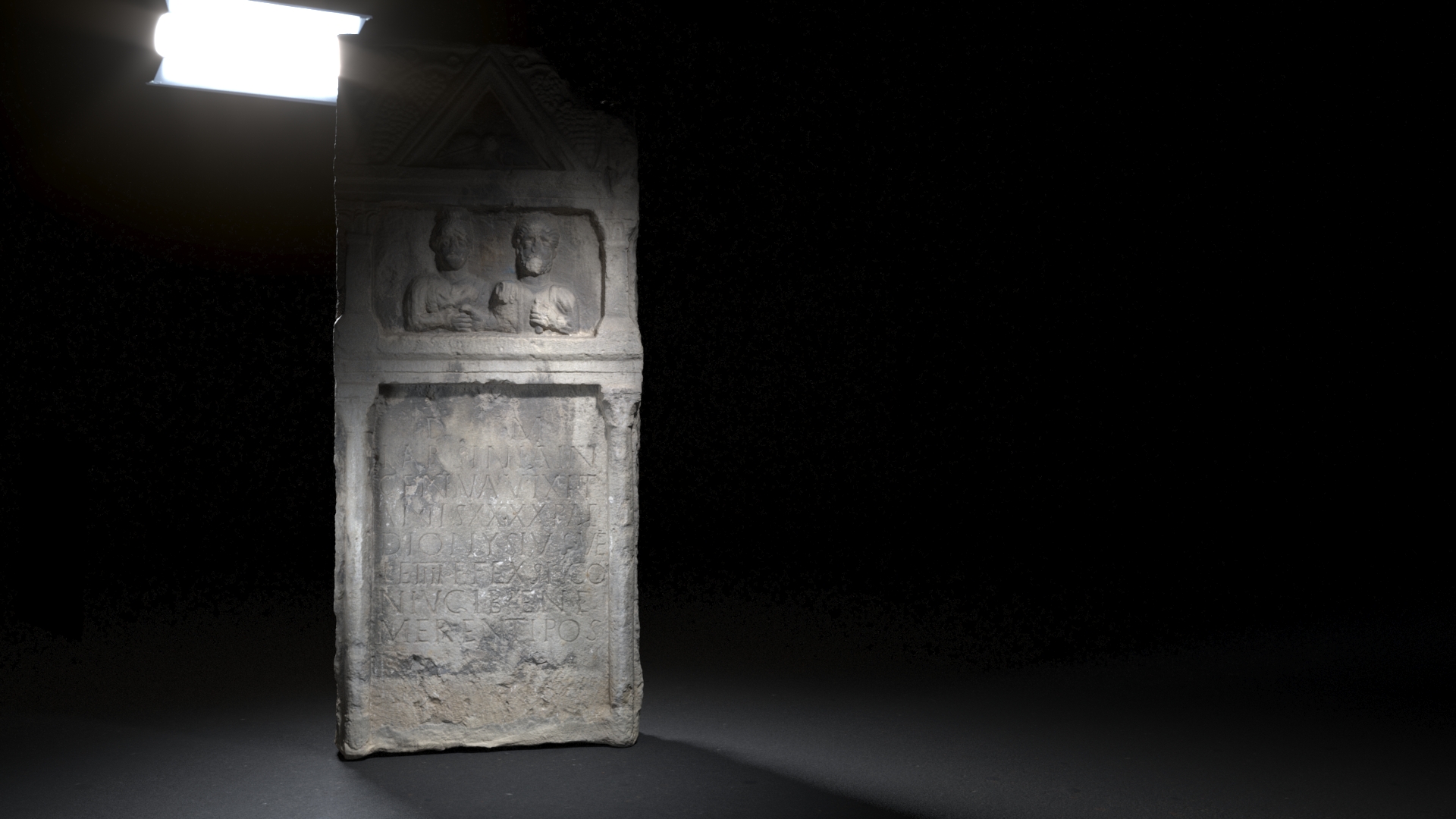 An ancient Roman funerary stele featuring a recessed relief of two male figures within an arched frame above a Latin inscription, all carved in stone, displayed with top-down lighting against a dark backdrop.