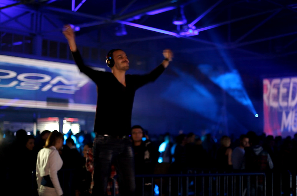 An individual in the foreground gestures energetically towards a vibrant, colorful backdrop, interacting with a music and visual effects installation that transforms movement into sound.