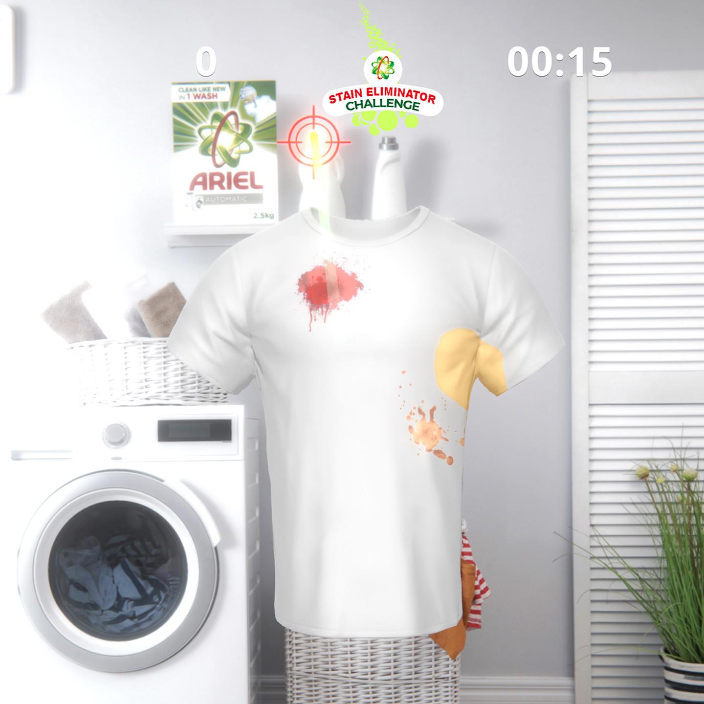 An engaging and bright virtual laundry setup displays the Ariel "Stain Eliminator" Challenge, a Kinect game. A white T-shirt displayed on a mannequin within a simulated laundry room shows a score of "0" and a timer set at "00:15". The shirt is stained with a red splash and a brown spill, with an Ariel product box visible on a shelf, promoting the stain-removing efficiency of Ariel laundry detergent through this interactive game.