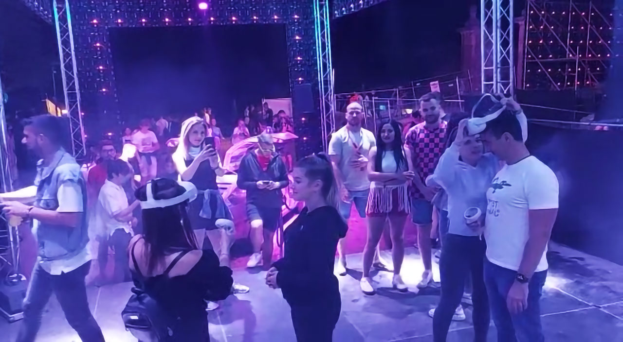 A dynamic scene at the EXIT Festival's VR Zone with festival-goers engaging in a lively party atmosphere. People are dancing and interacting with each other under purple-tinted lights, surrounded by stage equipment. This encapsulates the immersive experience created by Digital Mind, allowing participants to virtually step into the vibrant environment of the EXIT Festival as if they were present during the event itself.