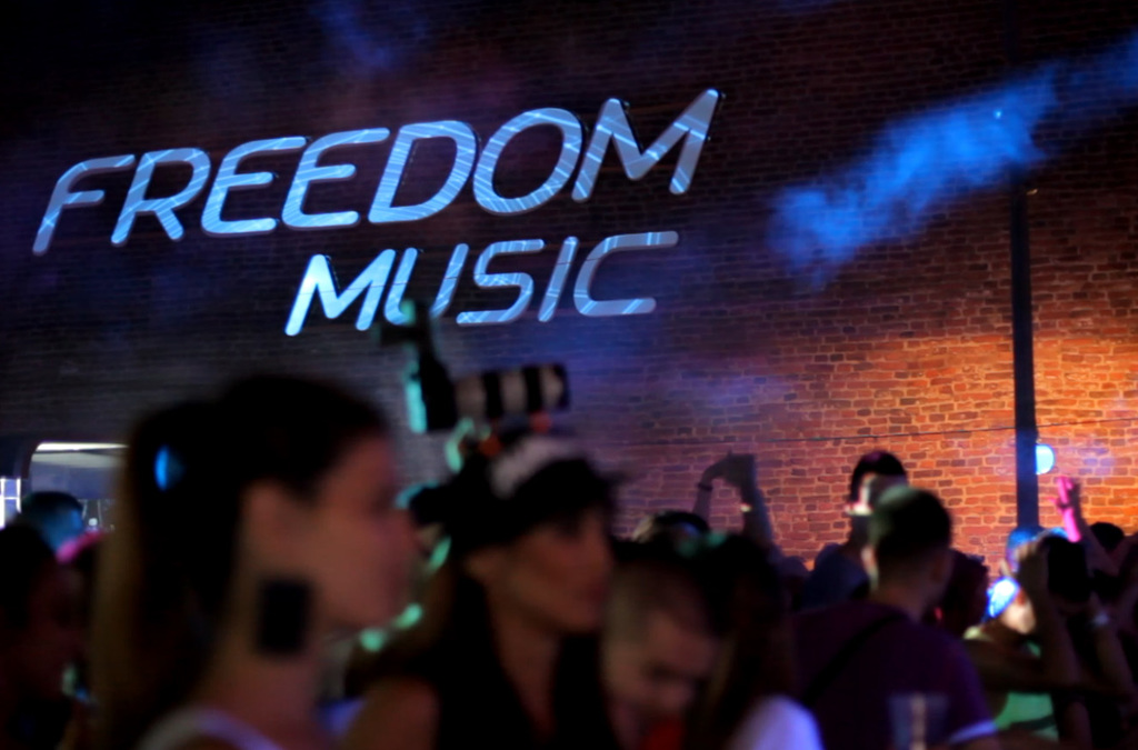 he words FREEDOM MUSIC projected onto a brick wall in stylized, glowing letters that appear to float in the air.