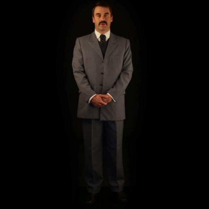 A man in a suit standing against a black background.